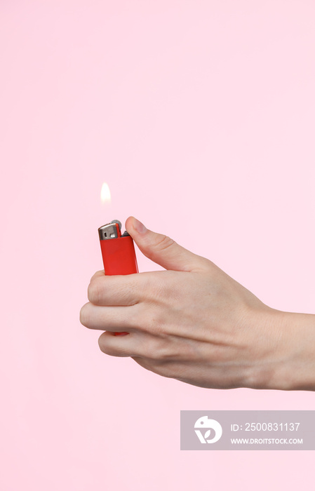 Flaming lighter in a female hand on a pink background