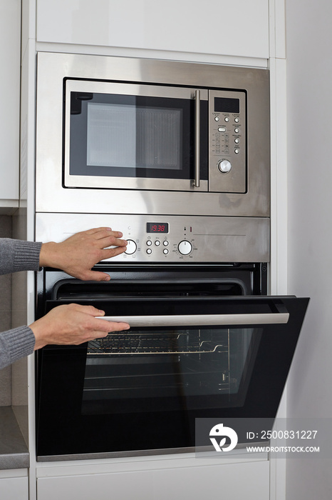 built in wall oven and microwave cabinet. Male hands open oven