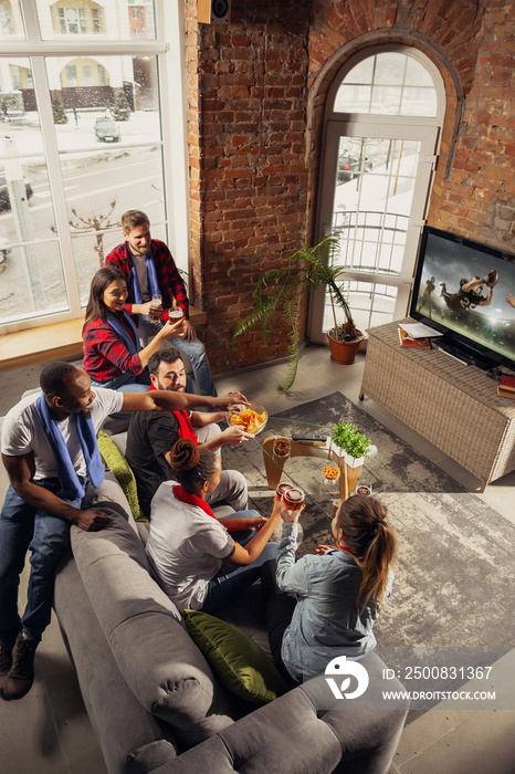 Excited group of people watching american football, sport match at home. Multiethnic group of emotional friend, fans cheering for favourite national team, drinking beer. Concept of emotions, support.