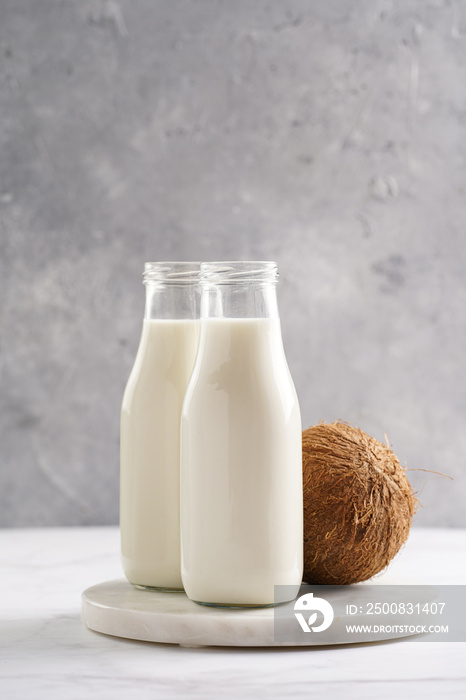 Two bottles with non-dairy milk and coconut on round marble board