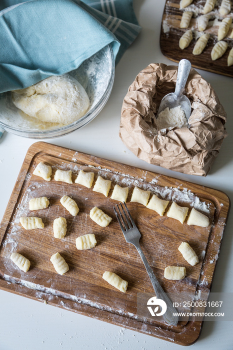 Forming gnocchi with fork on wooden board on white background.