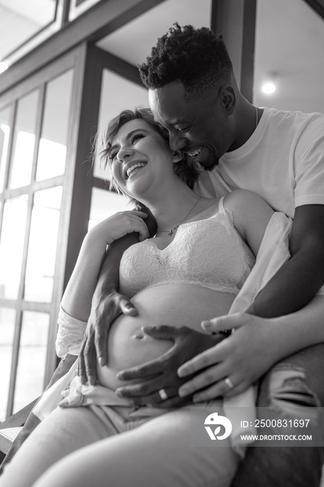 Happy african man and his caucasian pregnant woman have fun and laugh joyfully.