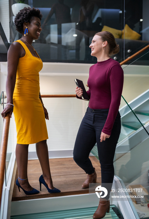 Diverse young businesswomen smiling and talking together on office stairs