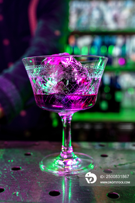 Close up of alcoholic cocktail, beverage, drink, prepared by professional barman in multicolored neon light. Entertainment, drinks, service concept. Modern bar, trendy neoned colors, copyspace.