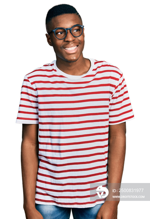 Young african american man wearing casual t shirt and glasses looking away to side with smile on face, natural expression. laughing confident.