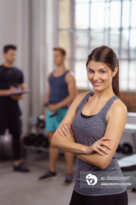 frau steht lächelnd mit verschränkten armen im fitnessstudio