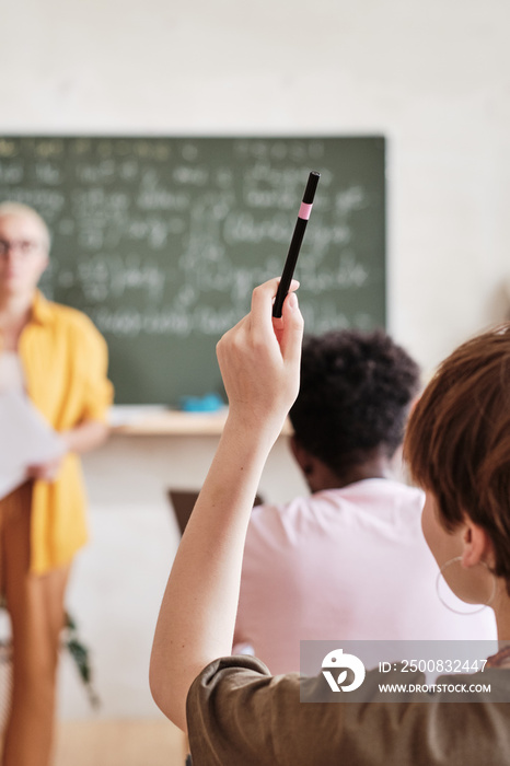 Rear view of student raising her arm up and answering during lesson at school