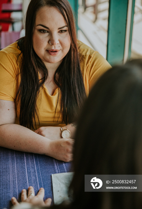 2 plus size Metis women sit across table and talk