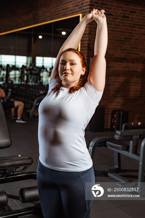 smiling overweight girl stretching with raised hands and looking at camera