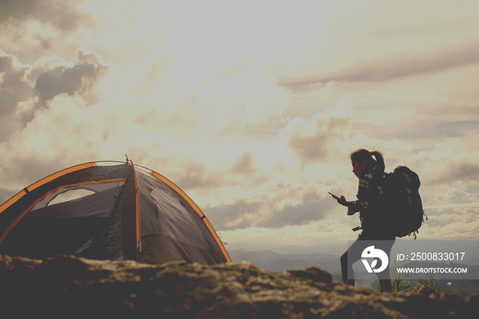 Girl hiker and  a tent and holding a mobile phone check GPS mountains in the background