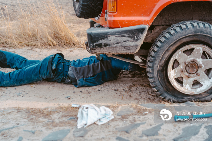 man lies under a 4x4 car on a dirt road