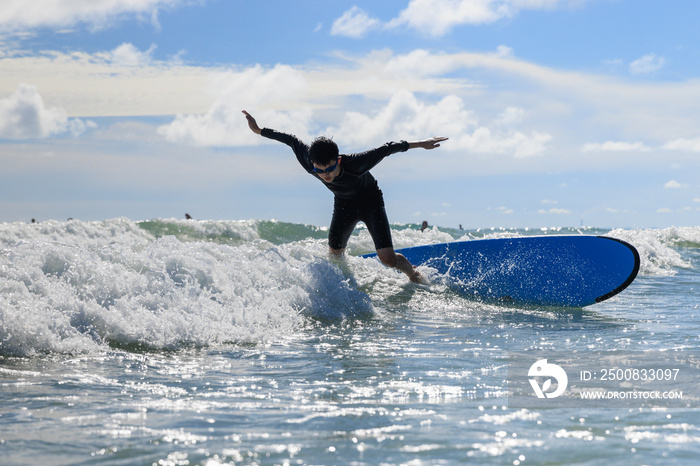 Young boy, new student in surfing, loses his body balance and falls from surfboard into the water during class.