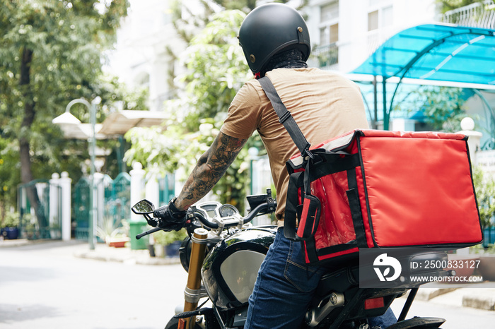 Courier with big thermal bag riding on motorcycle when delivering food to customers