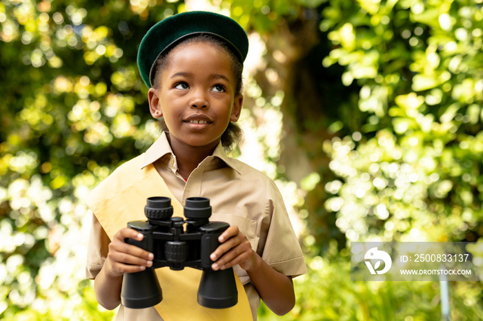 Cute african american scout girl in uniform holding binoculars in forest