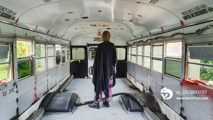 Wide angle shot of a man inside a bus in the process of being renovated. No seats, empty floor, ready for cleaning and re-purposing.