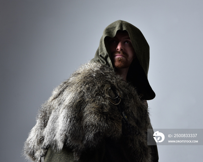 Close up  portrait of  young handsome man  wearing  medieval Celtic adventurer costume with hooded fur cloak,  isolated on studio background.