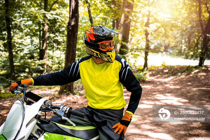 Portrait of professional dirt bike rider preparing for the motocross race through the forest.