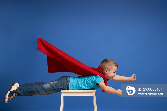 Boy in red superhero cloak flying on empty blue background