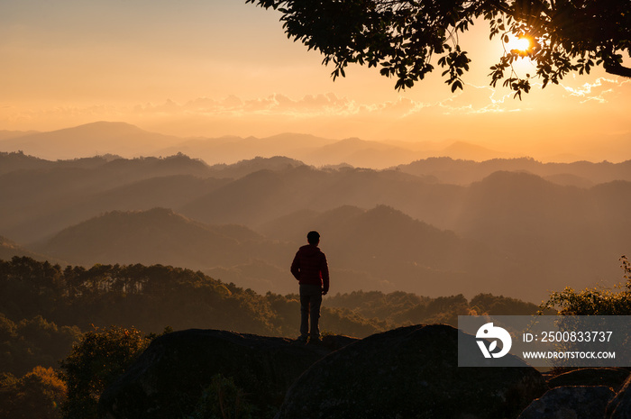 Young hiker man standing on top of mountain with the sun in the sunset