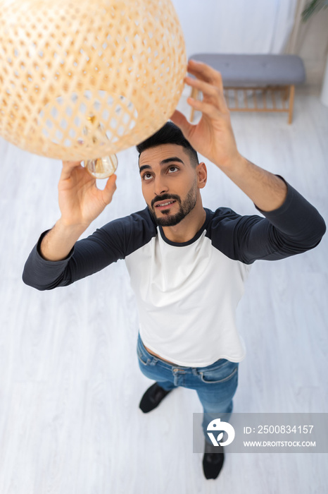 High angle view of smiling muslim man changing lightbulb in chandelier at home