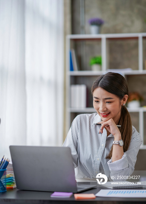 Confident successful businesswoman, freelancer or employee, sits at her work desk at home or in the office, uses a laptop, chats with colleagues, responds to emails, browses the Internet