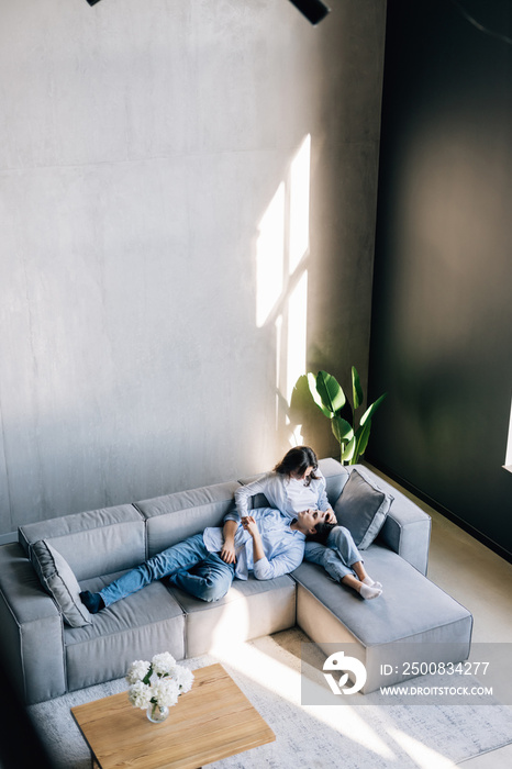 Loving couple holding hands, relaxing on cozy sofa in modern living room top view