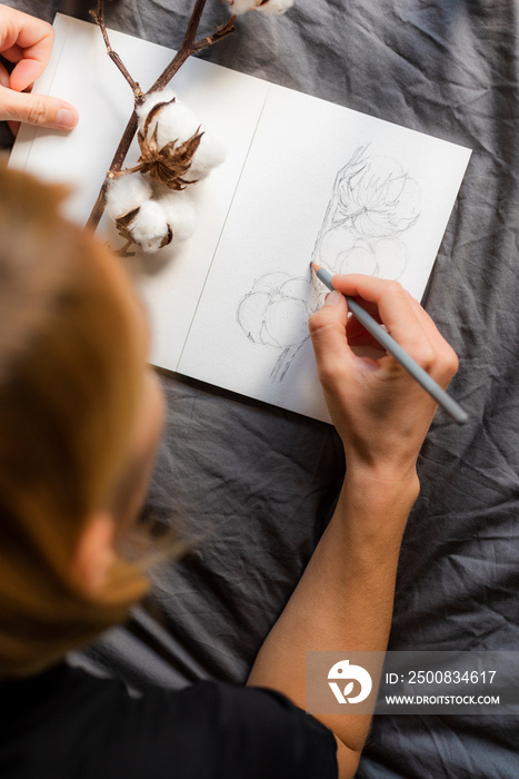 Girl draws a pencil sketch of cotton in a sketchbook. Hobbies and leisure.