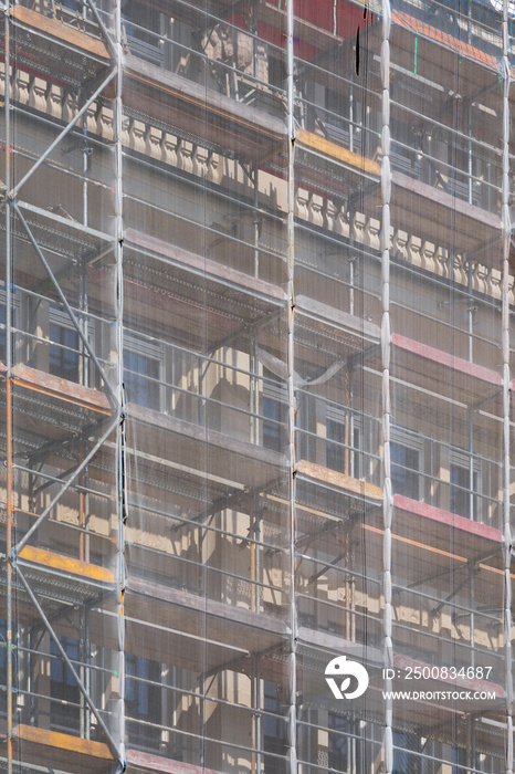A scaffolding covered by netting attached to a building during refurbishment.