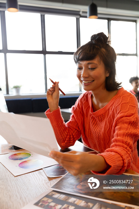 Smiling young creative asian businesswoman with photograph at desk in office