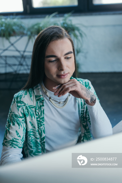 Young queer designer using blurred computer in office.