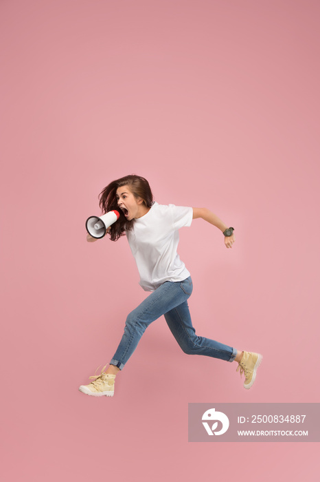 Beautiful young woman jumping with megaphone isolated over pink background. Runnin girl in motion or movement. Human emotions and facial expressions concept
