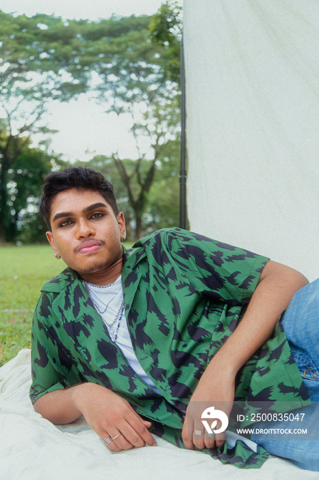 Malaysian Indian men in a group against a cloth backdrop in a park surrounded by trees, talking, laughing and sitting together