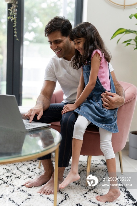 Father sitting with daughter and using laptop