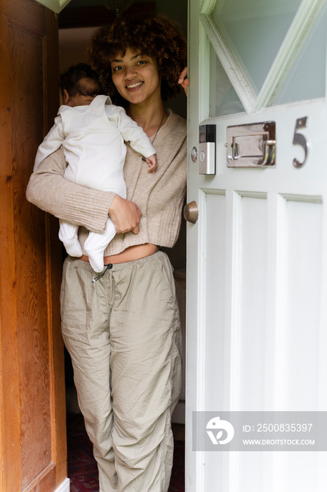 Mother holding baby daughter at home entrance