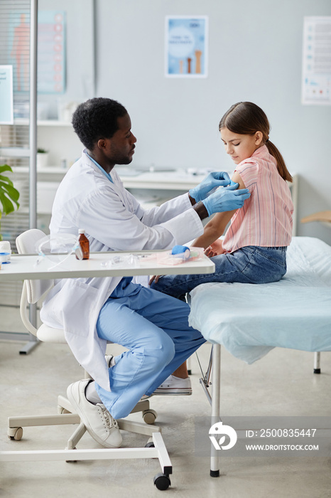 Vertical portrait of brave little girl getting vaccinated against COVID-19 in child vaccination clinic