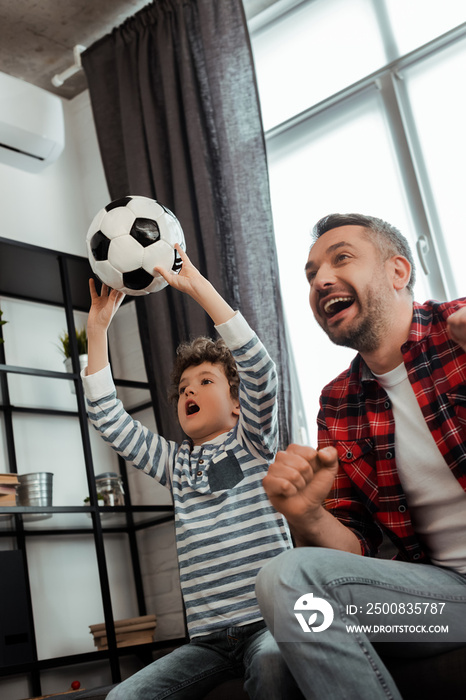 emotional kid holding football while watching championship with excited father