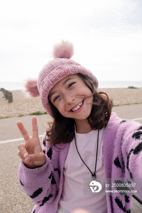 Portrait of smiling girl making peace gesture while taking selfie