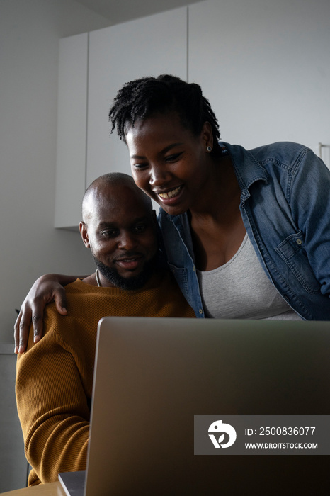 Man and pregnant woman looking at laptop in kitchen