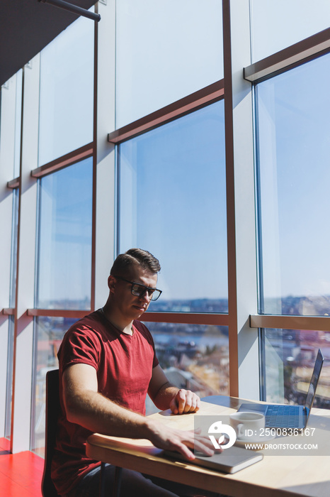 Smart software developer sitting at desktop in coworking space with laptop and creating publishing idea, using netbook for messaging and networking during freelance work