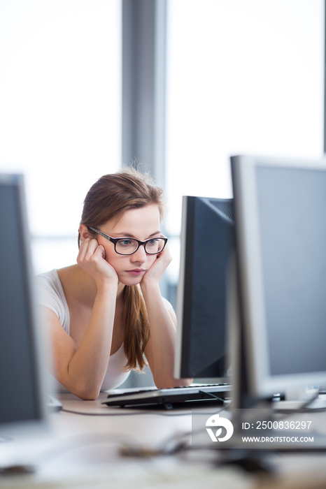 Pretty, female student looking at a desktop computer screen, learning unpleasant news about her exam results. University/office/school concept