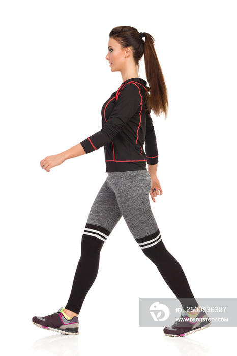 Walking Smiling Young Woman In Sports Clothes And Striped Leggings. Side View.