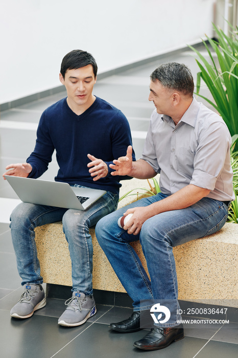 Mature entrepreneur offering mentoring advice to his young coworker with opened laptop