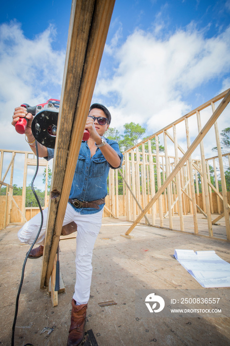 Mid adult woman using power tool, building her own home