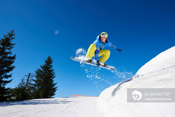 Male snowboarder, free rider flying on snowboard, jumping in air downhill on copy space background of blue sky and white snow on sunny winter day. Extreme sport, courage and confidence concept.