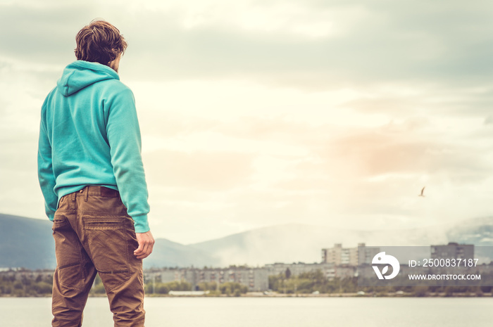 Young Man standing alone outdoor Travel Lifestyle concept with lake and city on background