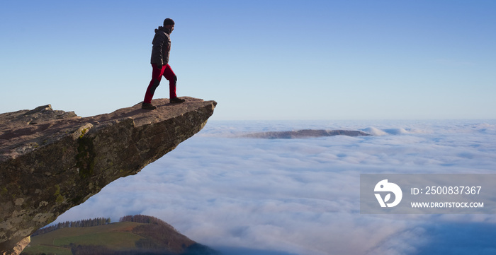 man standing on the cliff above the mountains and clouds