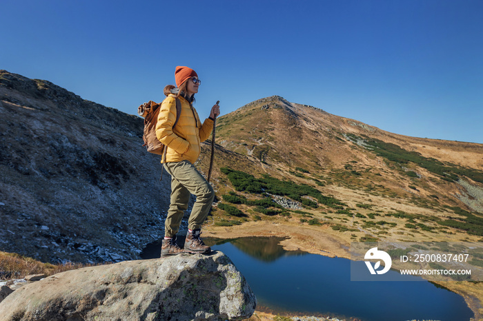 Portrait of a woman hiker standing on the slope of mountain ridge against mountains and lake