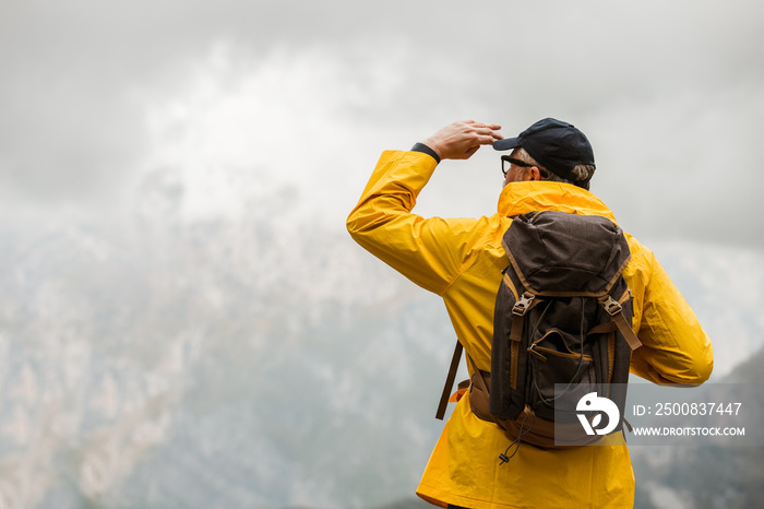 Middle age man traveler in raincoat and backpack enjoying view of mountains.