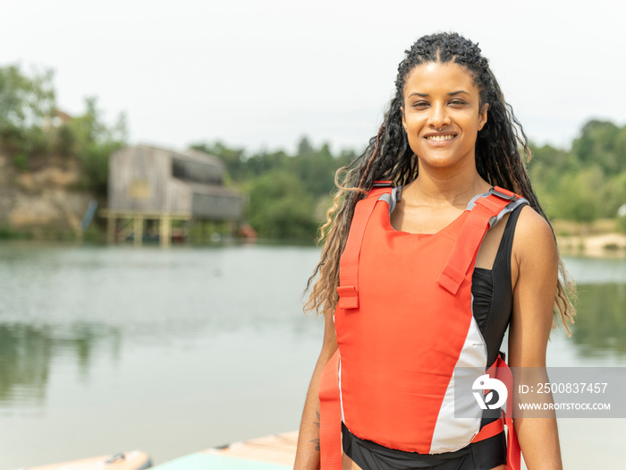 Portrait of smiling woman in life jacket standing by lake