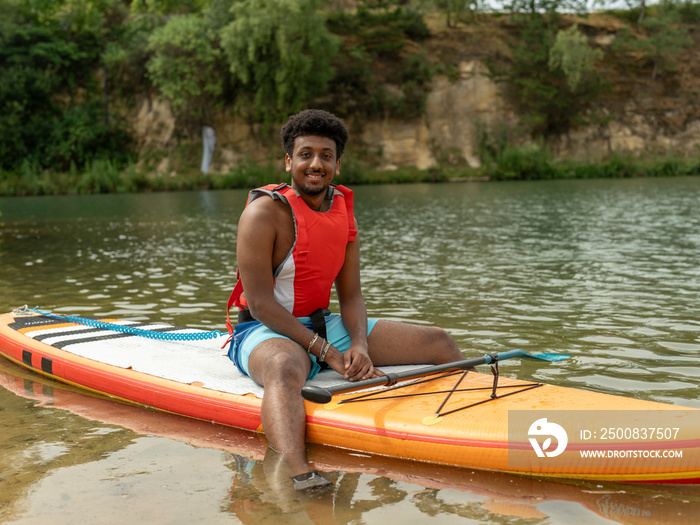 Portrait of young man sitting on paddleboard on lake